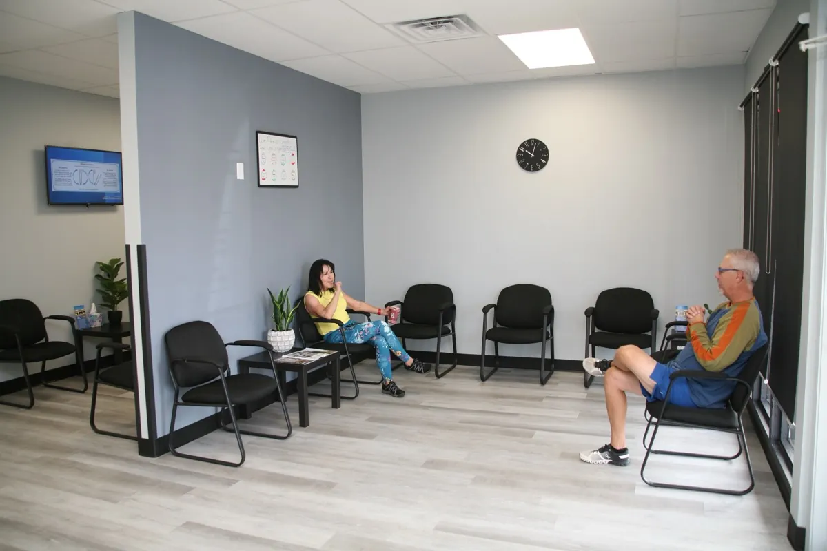 Waiting room at Frost Chiropractic in Tulsa with two patients seated and a wall clock